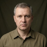 Smiling man with dark hair wearing a gray collared shirt.