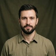 Smiling man with short brown hair and trimmed beard wearing a gray shirt.